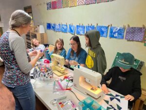 Photo of two volunteers assisting students on sewing machines
