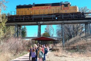 Forest school children walking along the Spring Creek Trail to Edora Park pass underneath a train overpass with a Union Pacific train going by